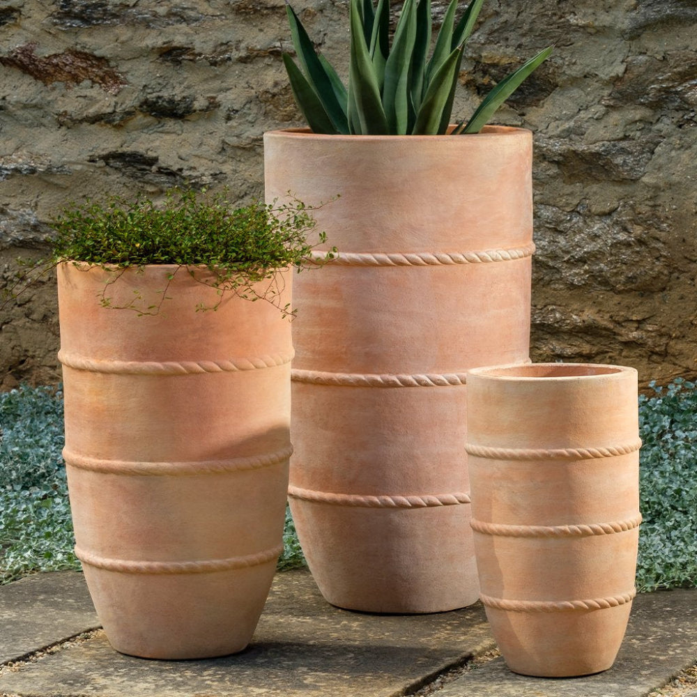 Three terracotta planters with plants against a stone wall.