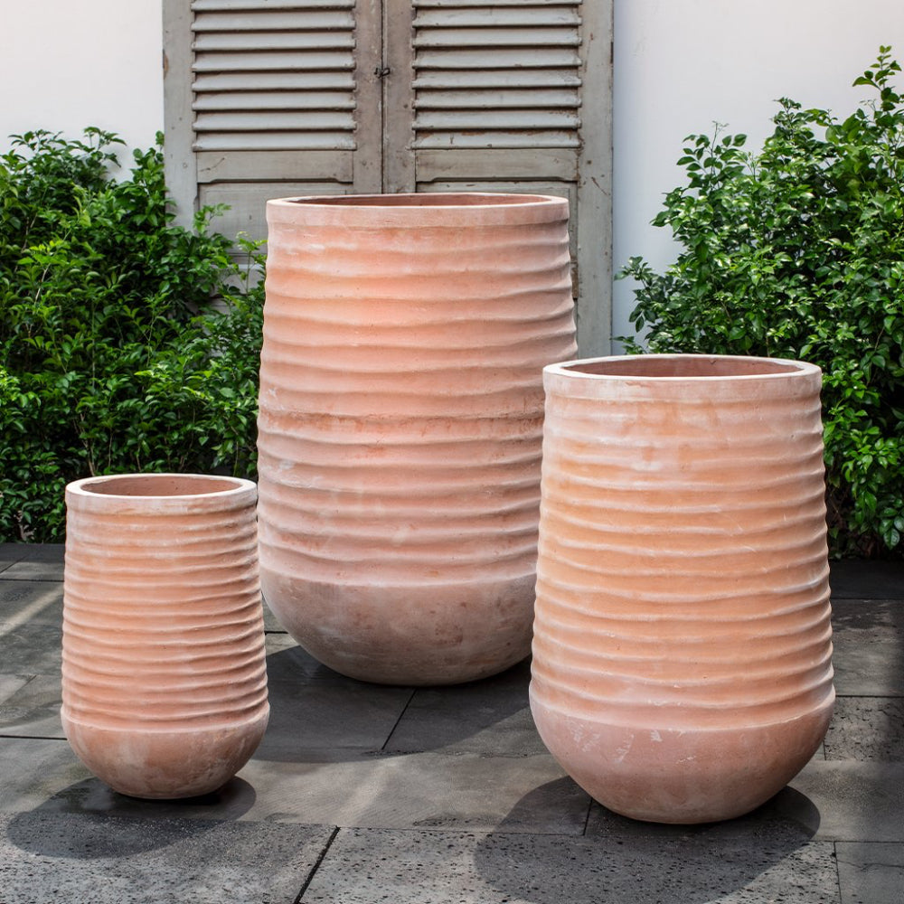 Three terracotta planters of different sizes on a patio with greenery in the background.