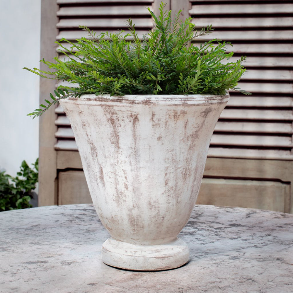 Decorative white urn planter with greenery on a wooden surface