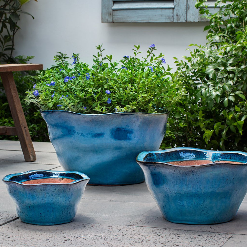 Three blue ceramic planters on a patio with greenery in the background