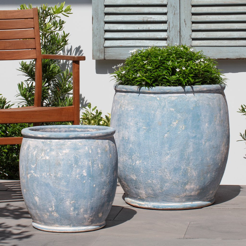 Two large blue ceramic planters with green plants on a wooden deck.