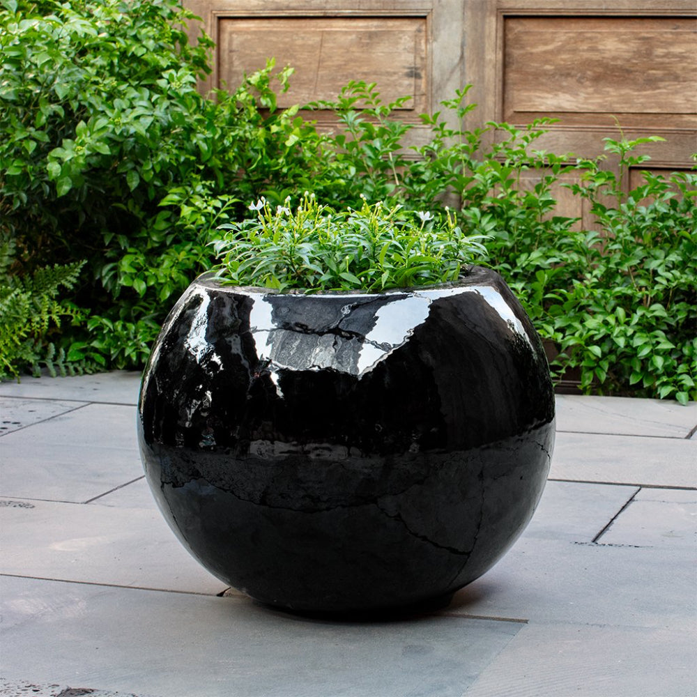 Black glossy spherical planter with green plants on a stone patio