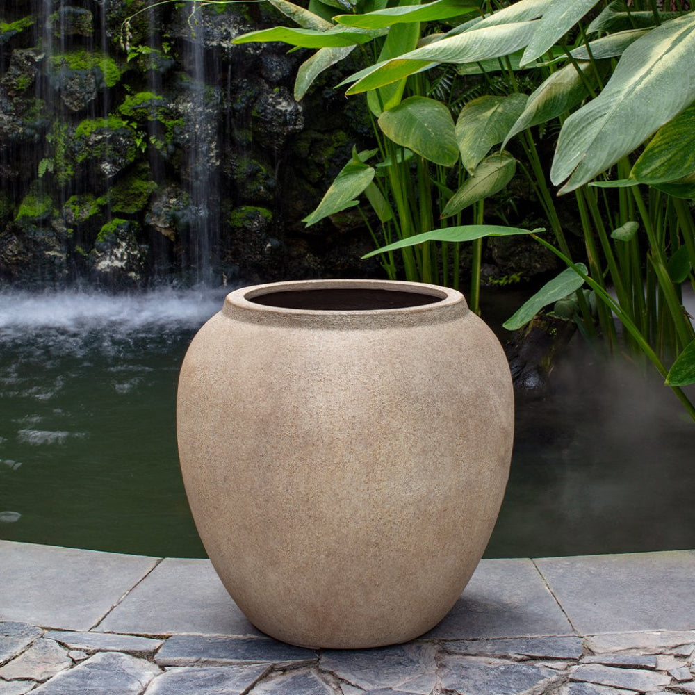 Beige pot on a stone surface with a water feature and greenery in the background