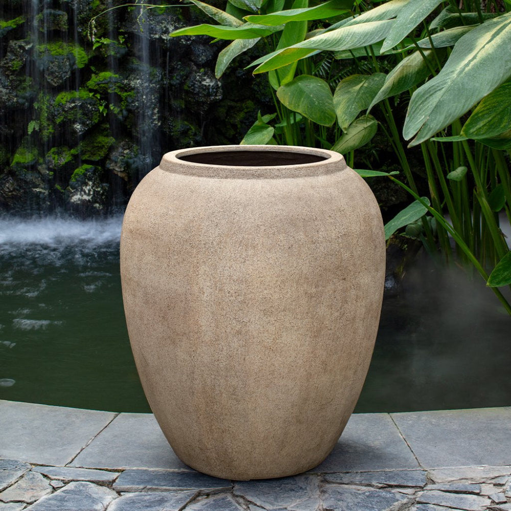 Beige ceramic pot on a stone patio with a water feature and greenery in the background