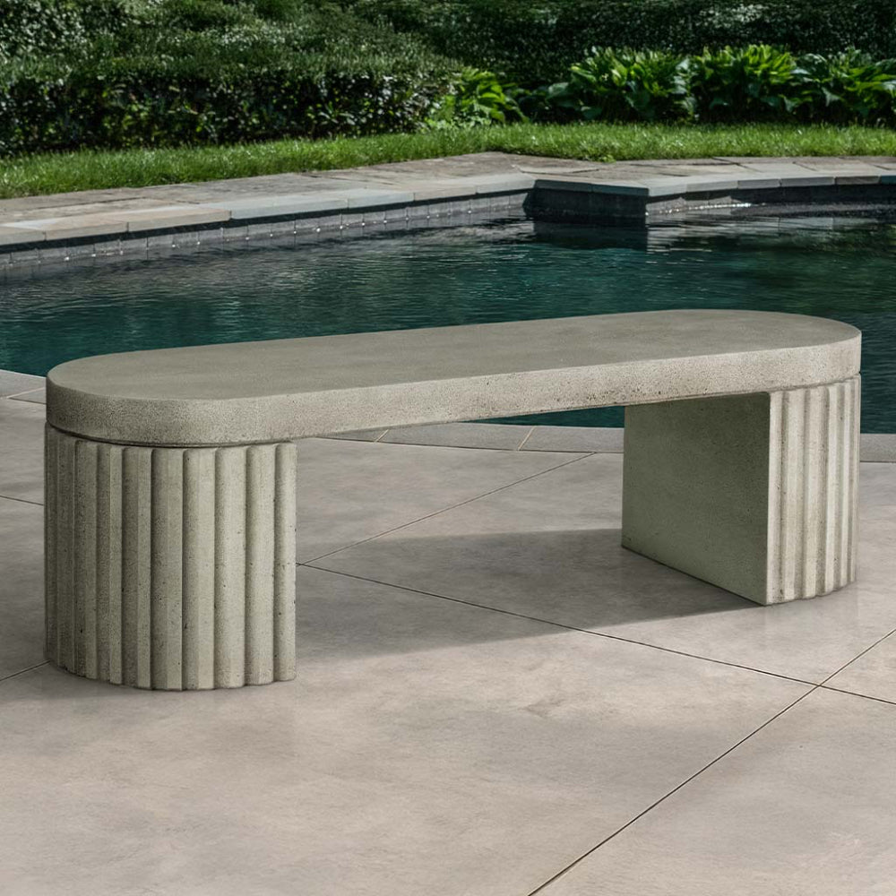 Fluted cast stone bench by a pool with greenery in the background