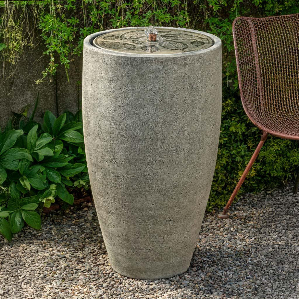 Cast stone water fountain with decorative top in a garden setting