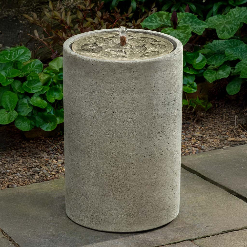 Cylindrical cast stone water fountain with decorative top on a patio