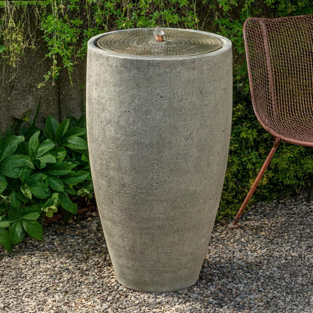 Cast stone water fountain with a decorative top in a garden setting