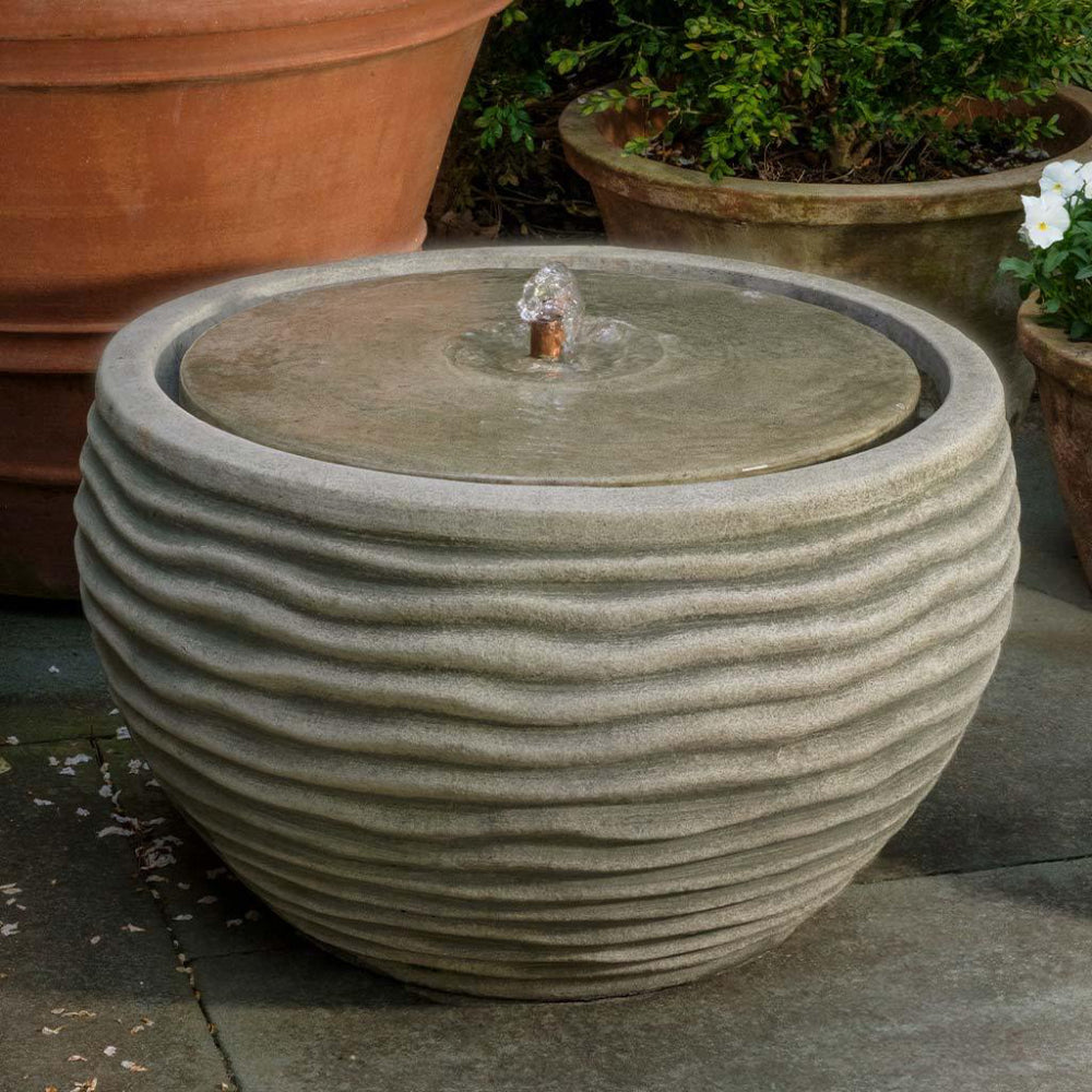 Decorative cast stone water fountain with potted plants in the background