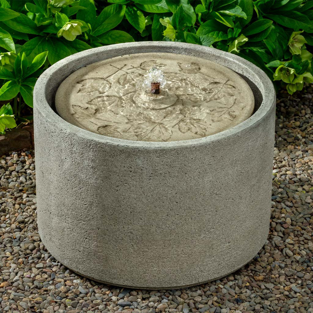 Decorative stone water fountain with intricate leaves design on a pebble ground