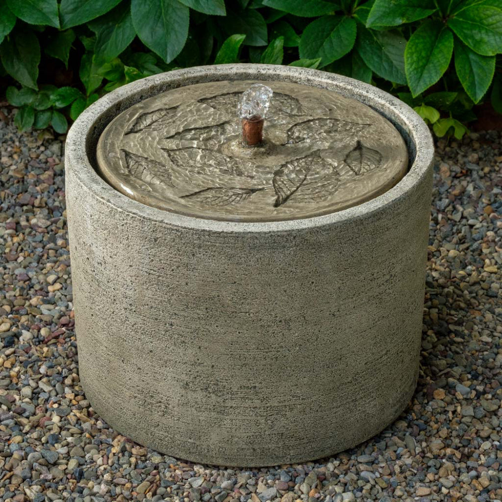 Cast stone garden fountain with leaf design on a gravel surface