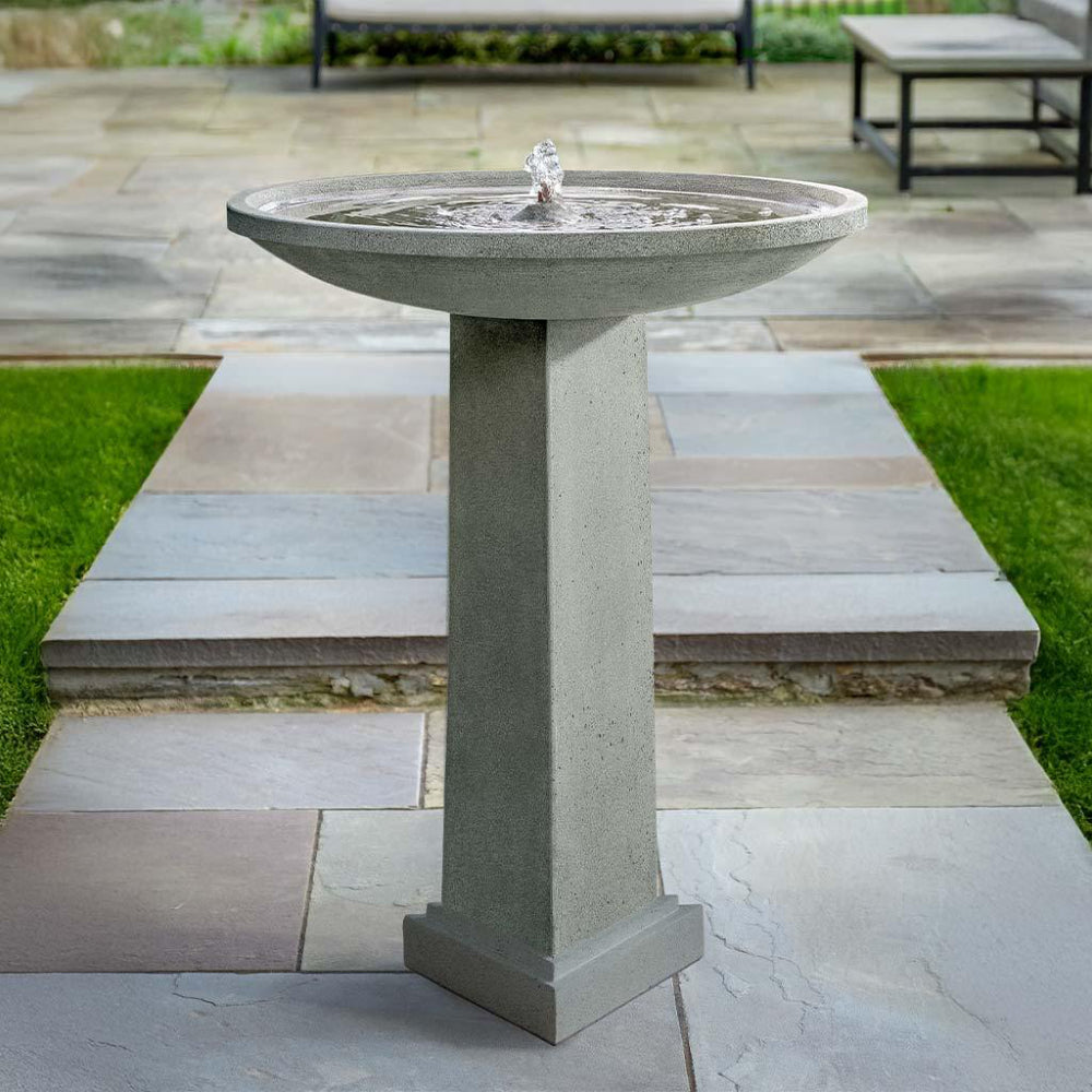 Cast stone bird bath fountain on a patio with grass and steps in the background