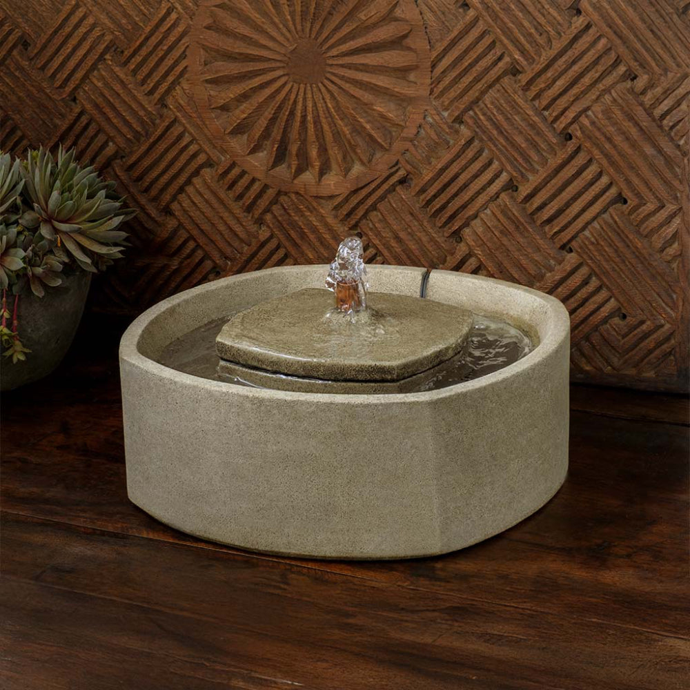 Cast stone water fountain with decorative stone top on a wooden surface