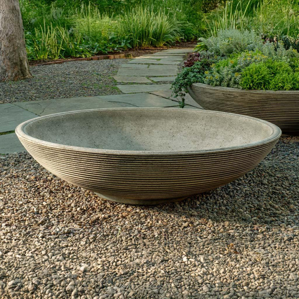 Decorative stone bowl on a gravel surface with a garden background