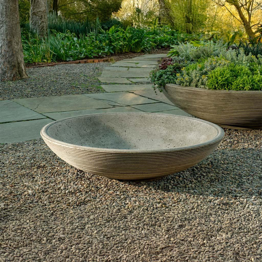 Two cast stone bowls on a gravel path with a garden background