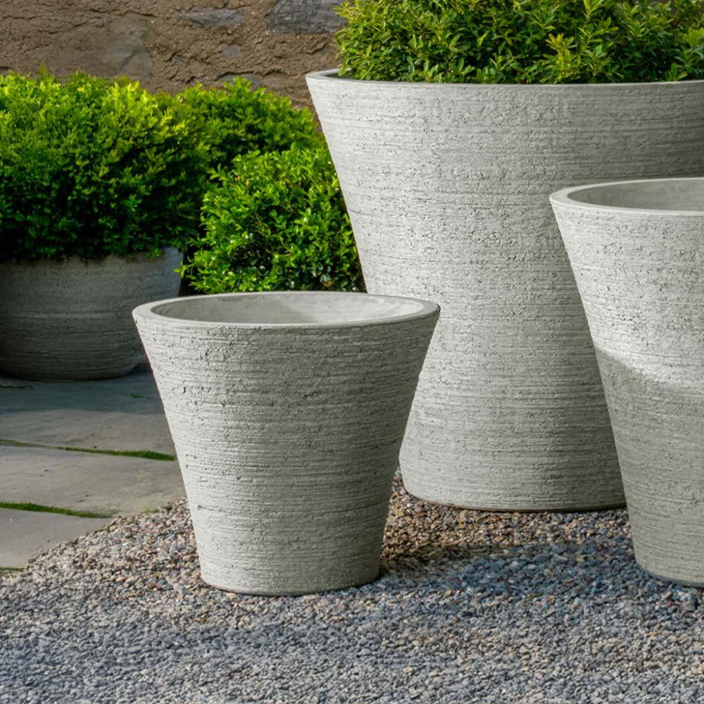 Set of gray stone planters with green plants against a stone wall.