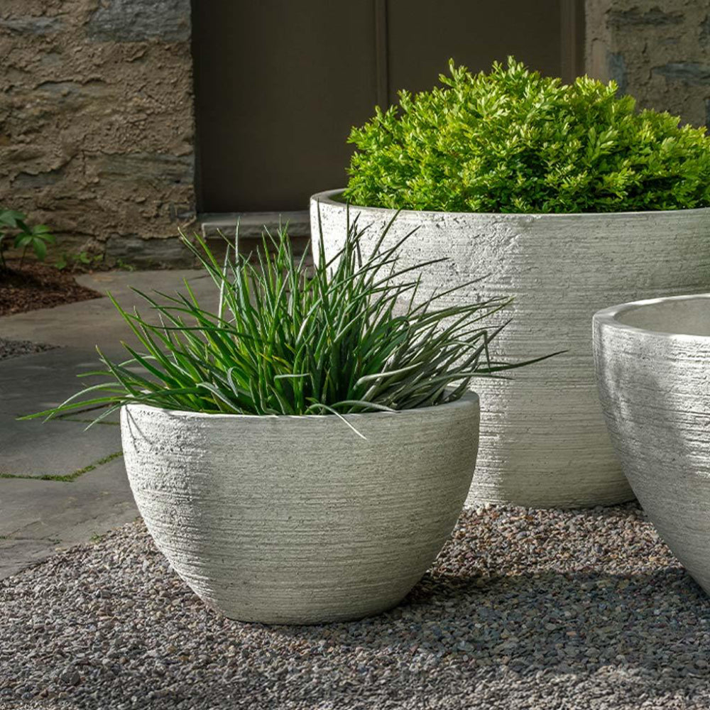 Decorative stone planters with green plants against a stone wall.