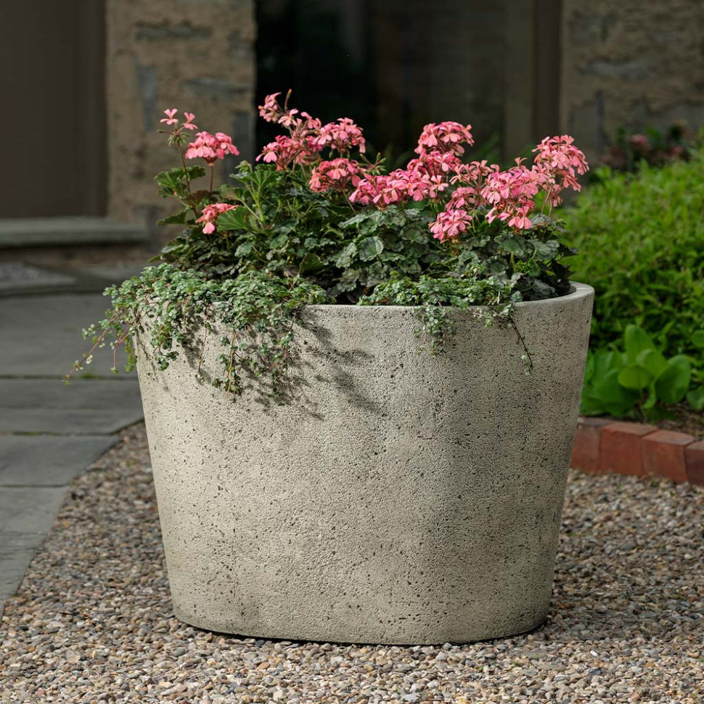 Concrete planter with pink flowers on a gravel surface