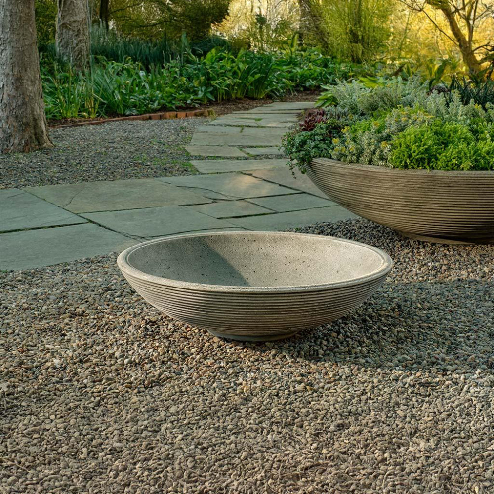 Two stone bowls on a gravel path with a garden background