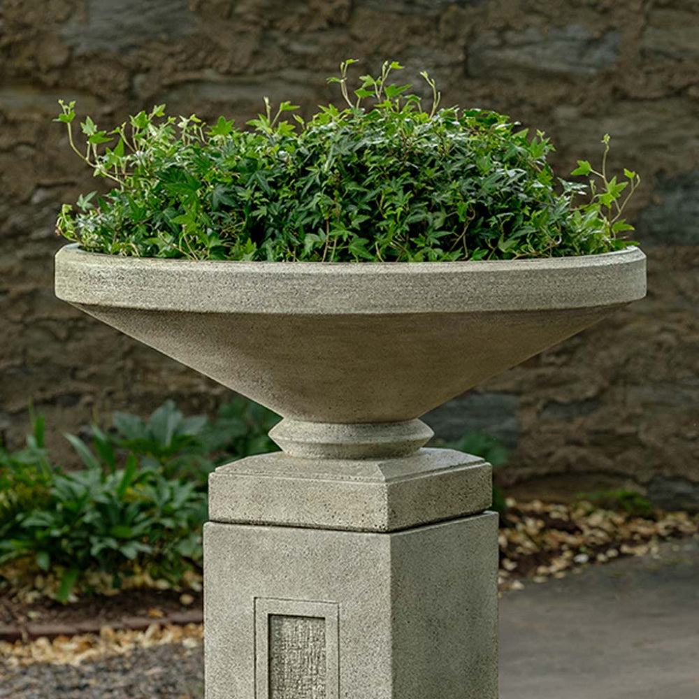 Decorative stone planter with green ivy against a stone wall background