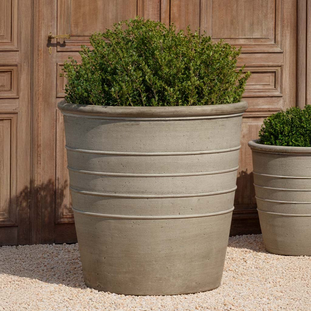 Large cast stone planter with green plants against a wooden background