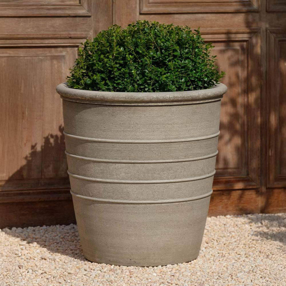 Large cast stone planter with green plant against a wooden background