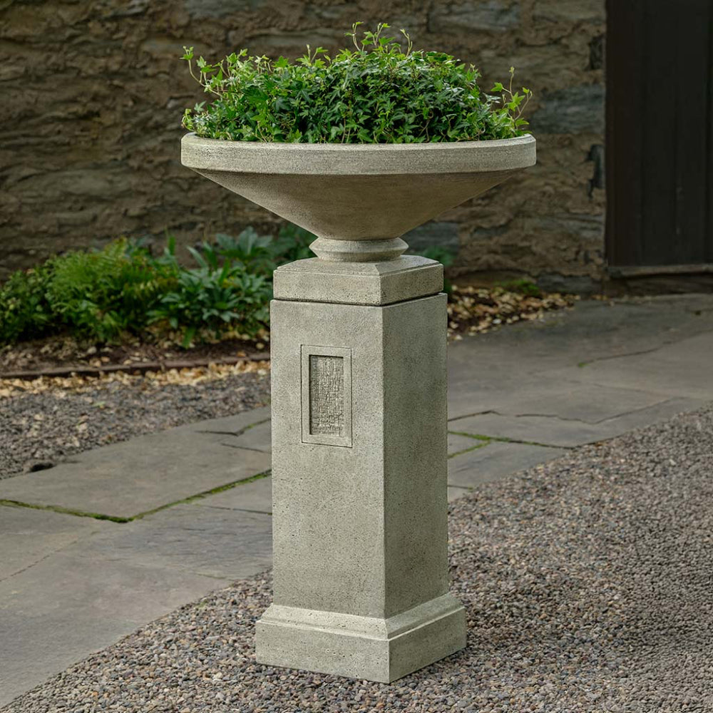Decorative cast stone urn planter on a pedestal with greenery on a stone patio